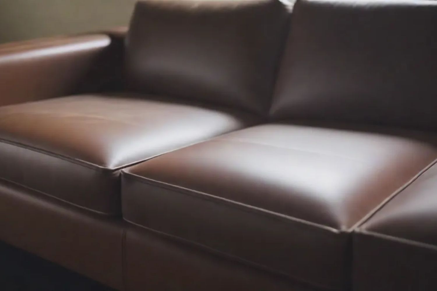 Close-up of a sleek brown leather sofa with smooth cushions and minimalist design, evoking comfort and modern elegance.