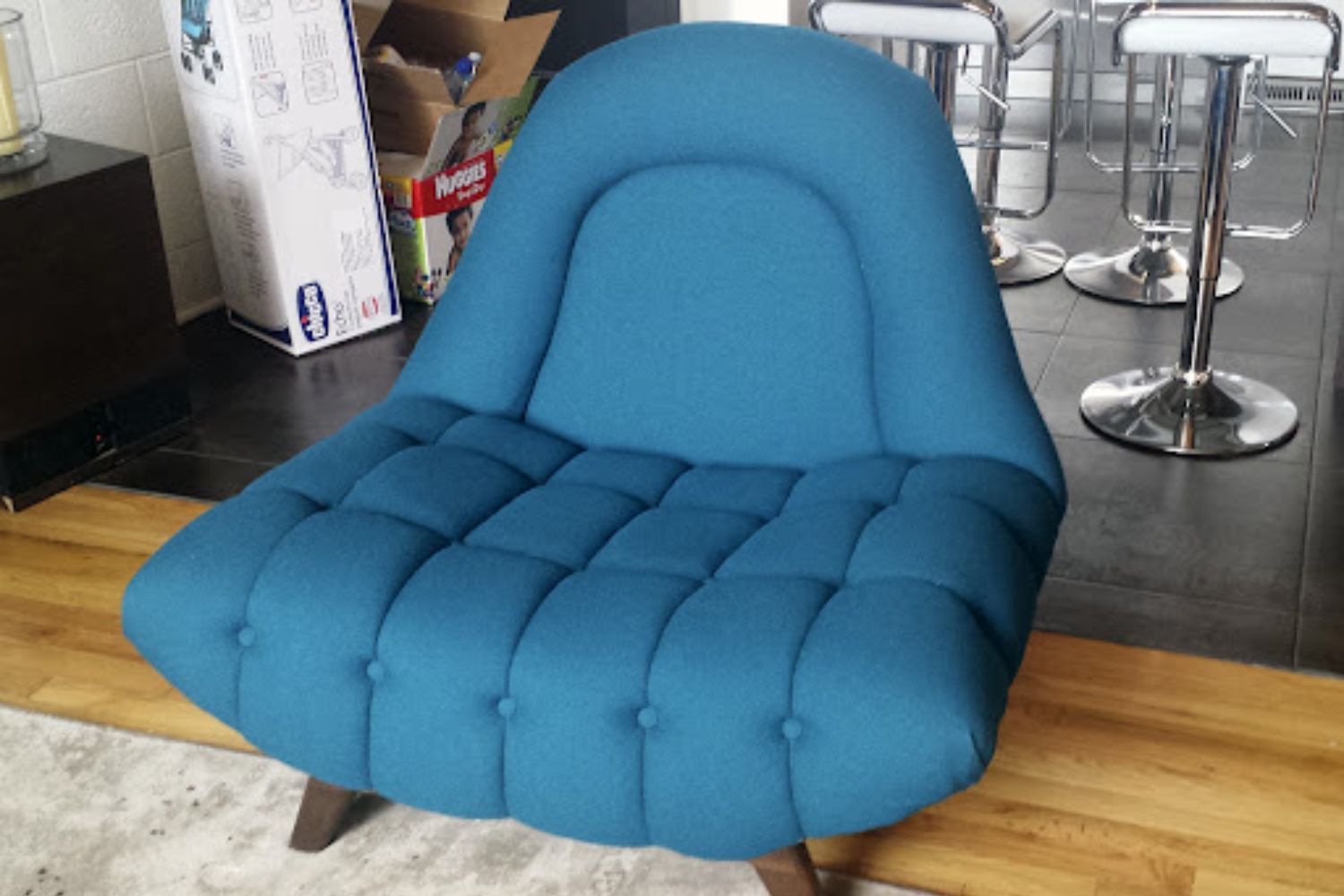 A modern tufted teal chair with a curved backrest and wooden legs, placed in a contemporary living room setting.