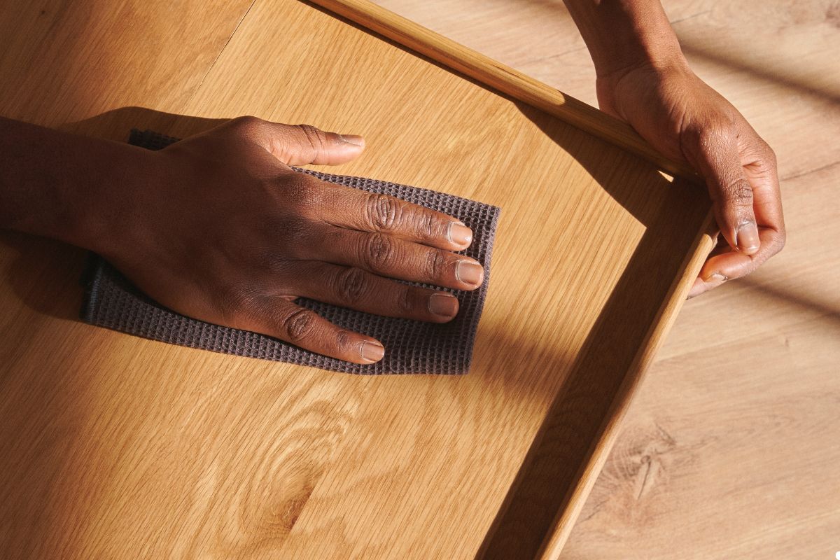 A person using a cloth to clean a wooden table, ensuring its surface is spotless and well-maintained. 