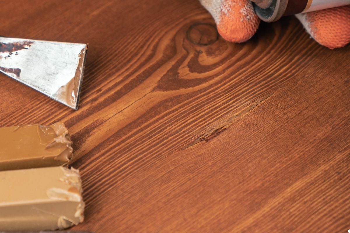 An individual applies paint to a wooden surface using a brush, showcasing creativity in a bright environment.